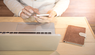 Image d'une personne utilisant un cellulaire devant un ordinateur portable ouvert sur un bureau