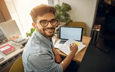 Image d'un étudiant souriant à un petit bureau avec un ordinateur