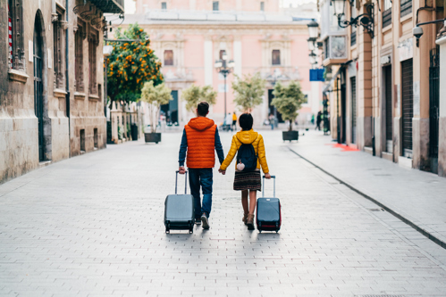 couple walking along street pulling luggage