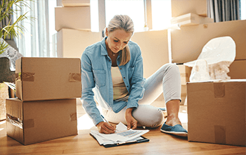 Image of woman completing paperwork on the floor surrounded by moving boxes