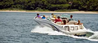 Family taking a ride in their boat on a lake with the shorline and trees in the background