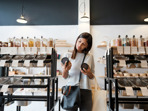 woman standing near bulk bins in grocery store comparing two jars