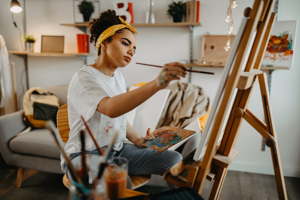 woman painting on canvas on easel in her bedroom