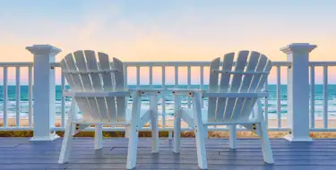 Image of chairs on a deck overlooking a beach at sunset