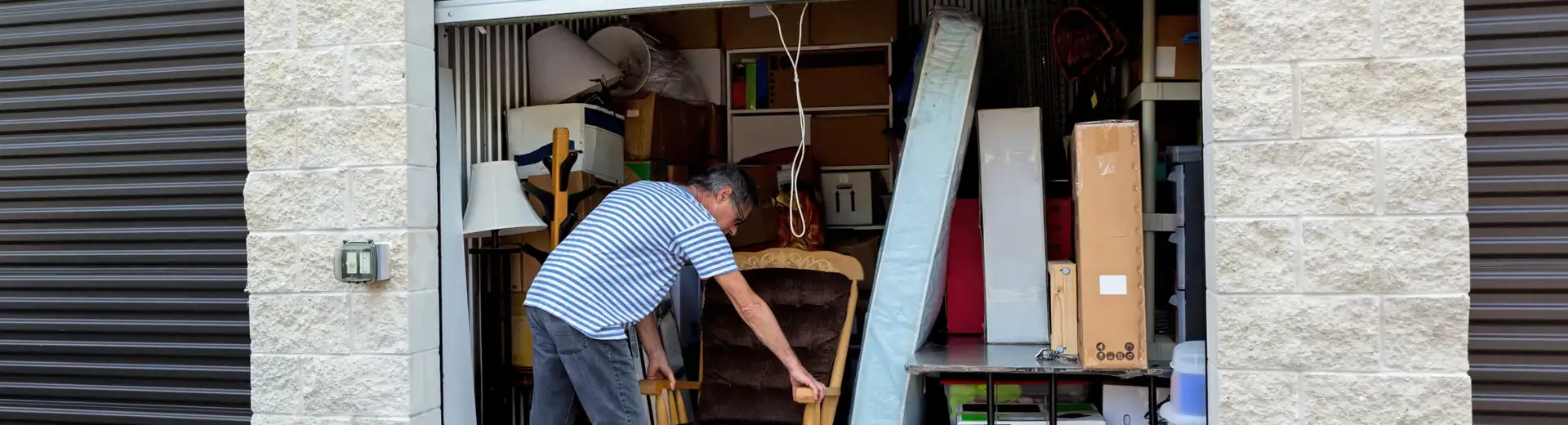 man storing a rocking chair in crowded self-storage unit