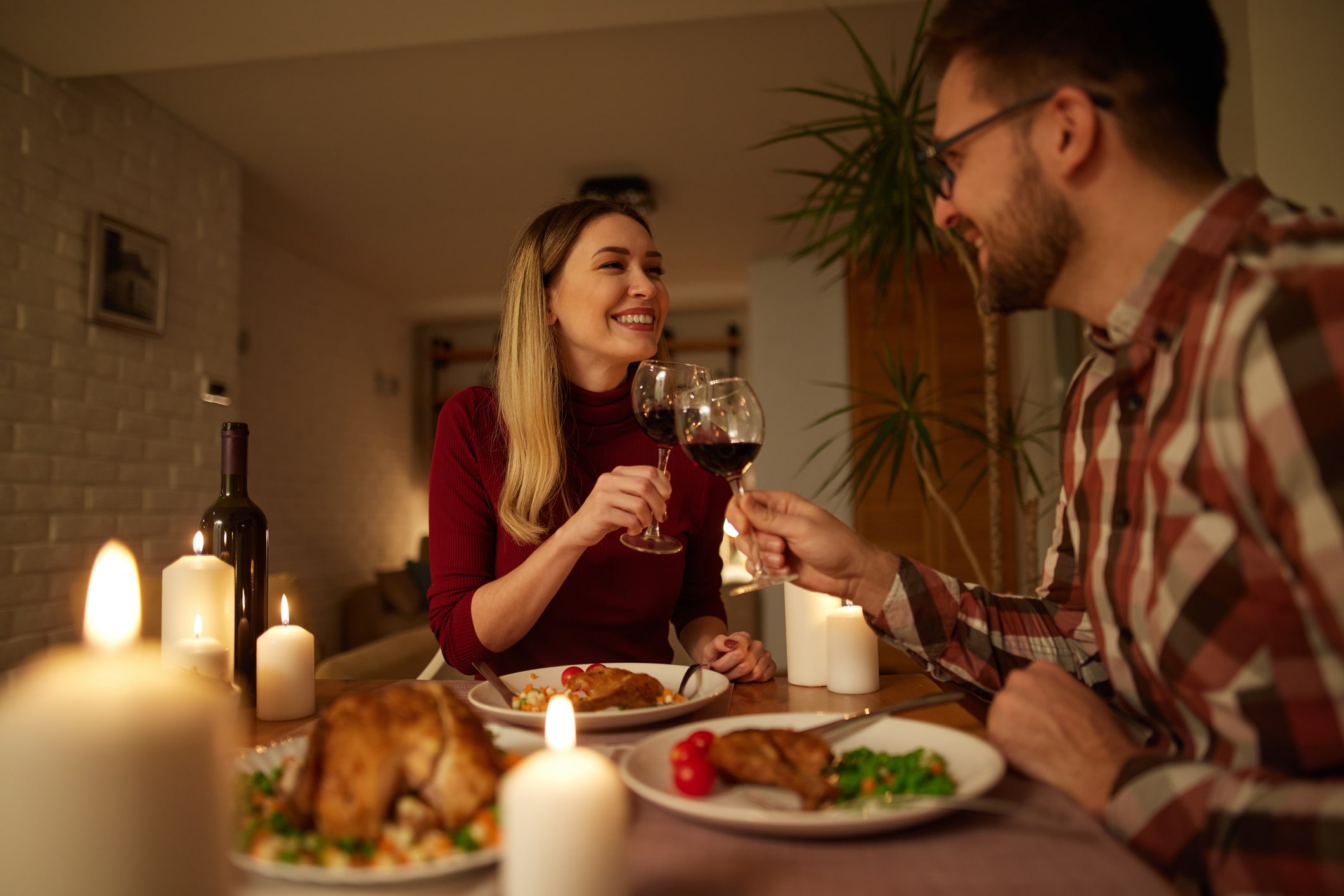 couple clinking wine glasses together during candlelit dinner at home