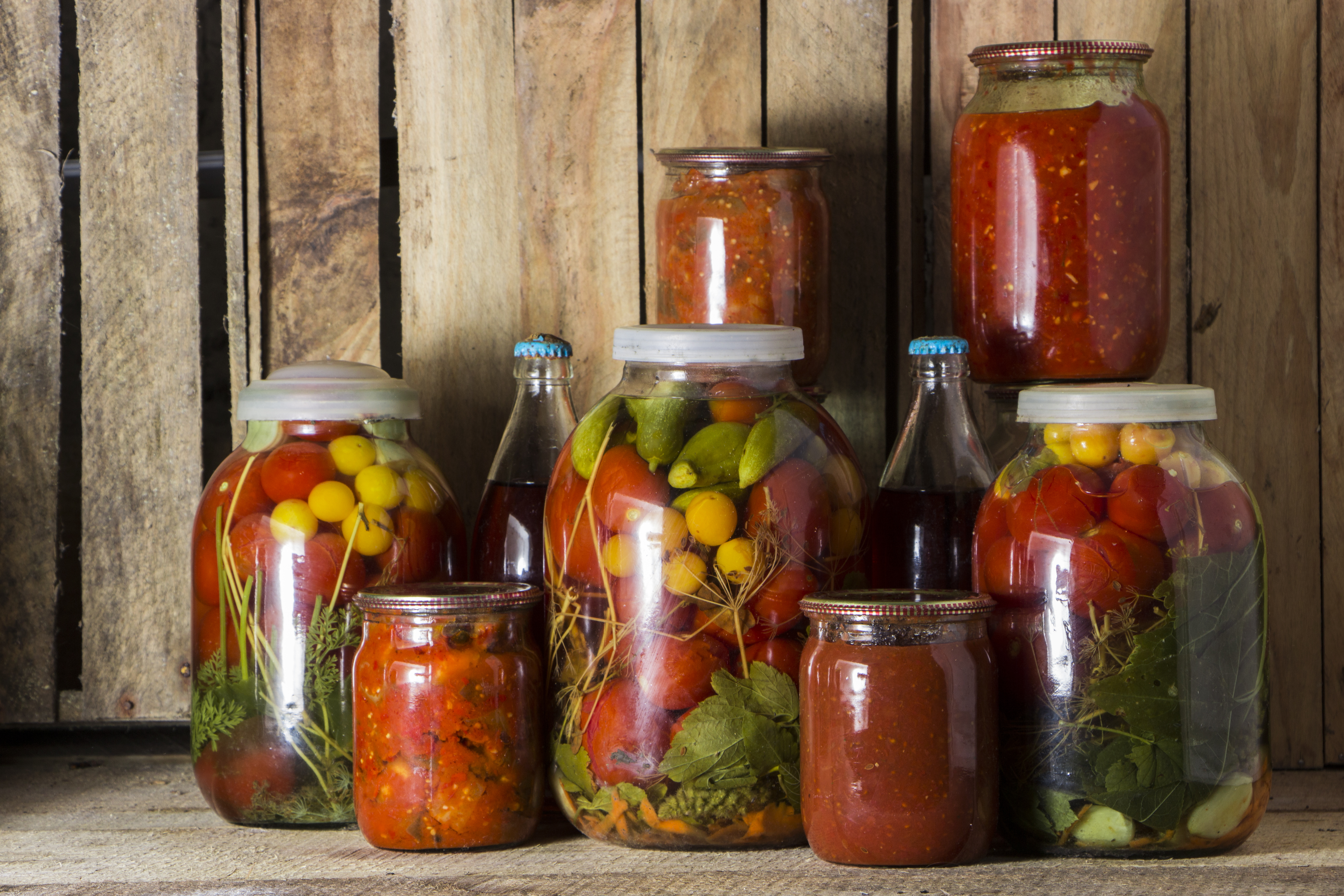 assortment of glass jars filled with preserved vegetables and sauces on a wooden surface