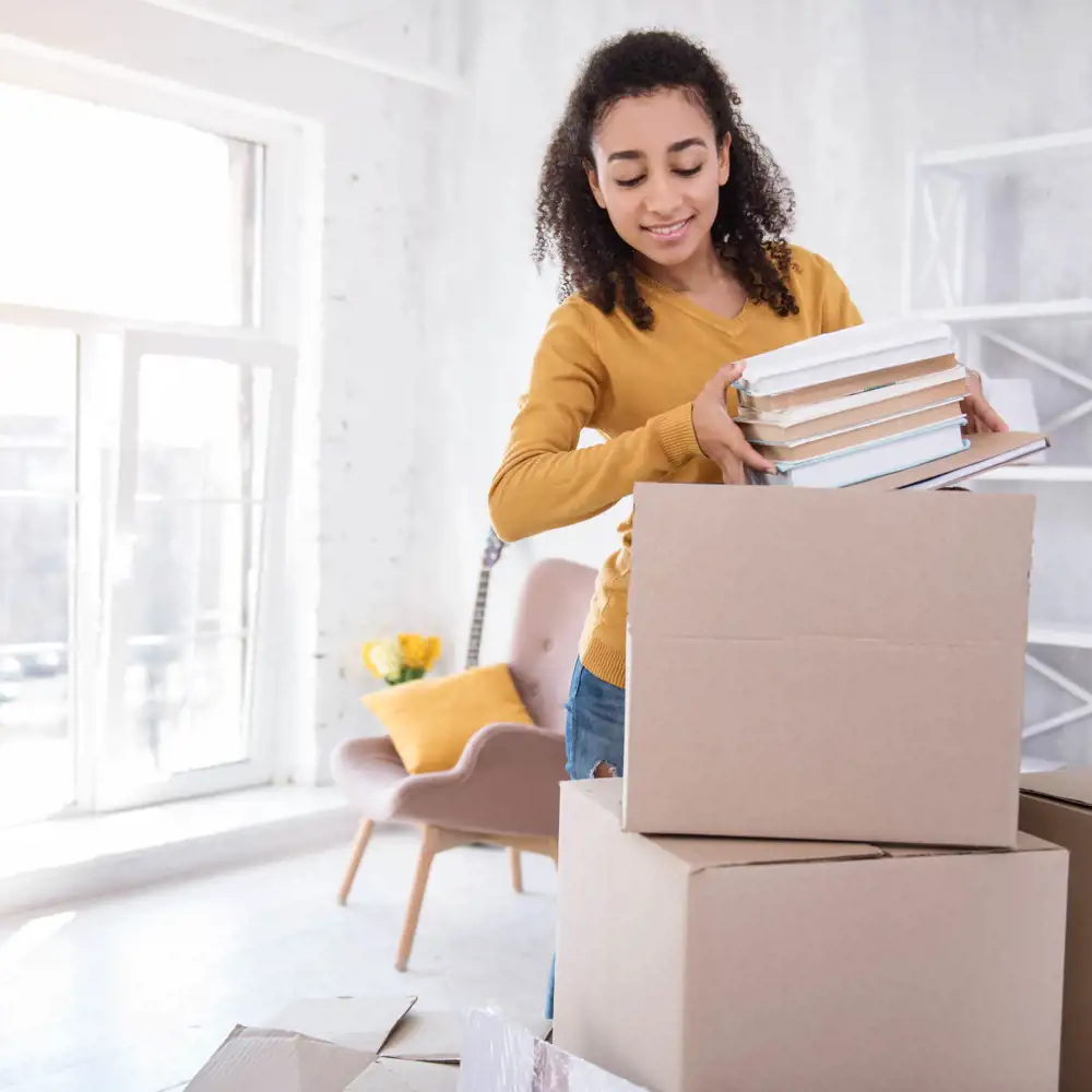 college student placing books into a cardboard moving box