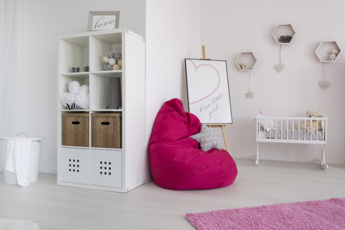 coin de chambre de bébé minimaliste avec étagère blanche, pouf rose et petit berceau