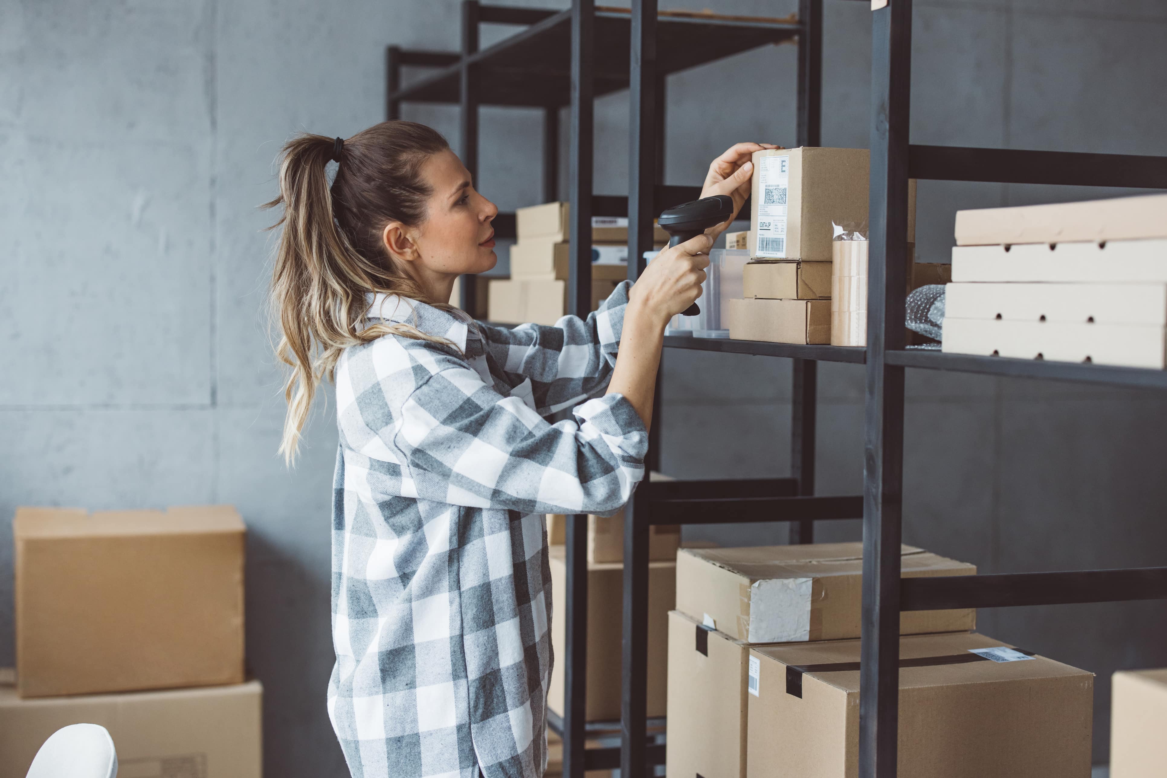 woman scanning barcode of box on shelving unit in storage