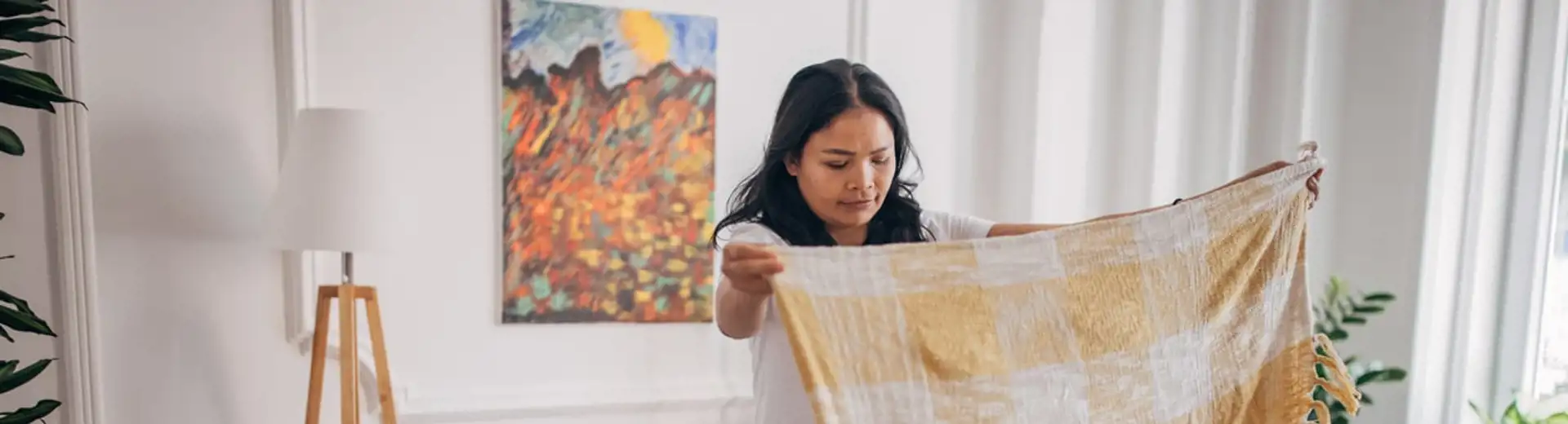 woman folding thin blanket next to couch in living room