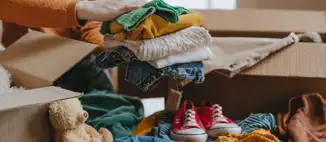 woman placing folded clothes into box for summer storage