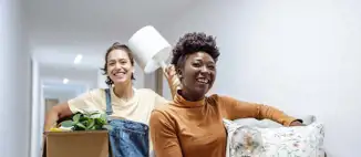 two college students smiling as they walk through dorm hallway with boxes of items