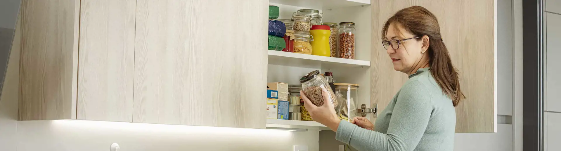 femme examinant un bocal d'aliments secs dans une armoire de cuisine