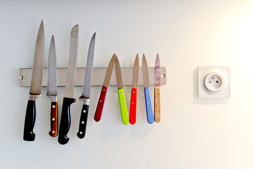 kitchen knives arranged on a magnetic wall strip next to a power outlet