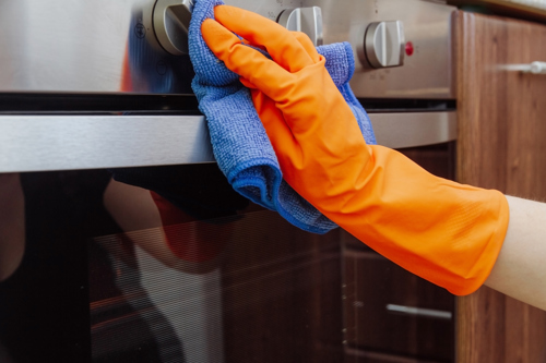 person wearing dish glove wiping down oven surface with diy stainless steel cleaner