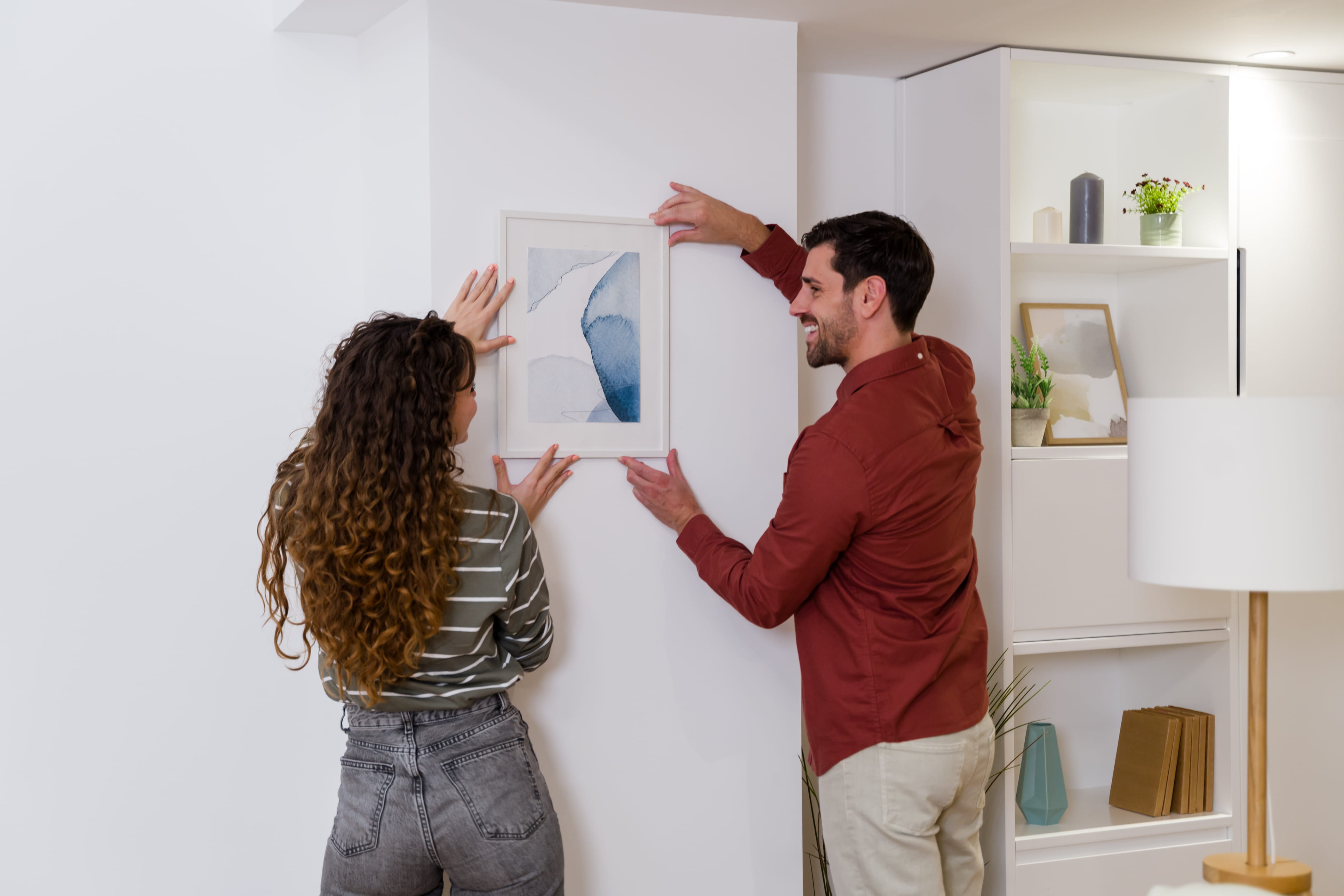 man and woman placing framed watercolor painting on wall