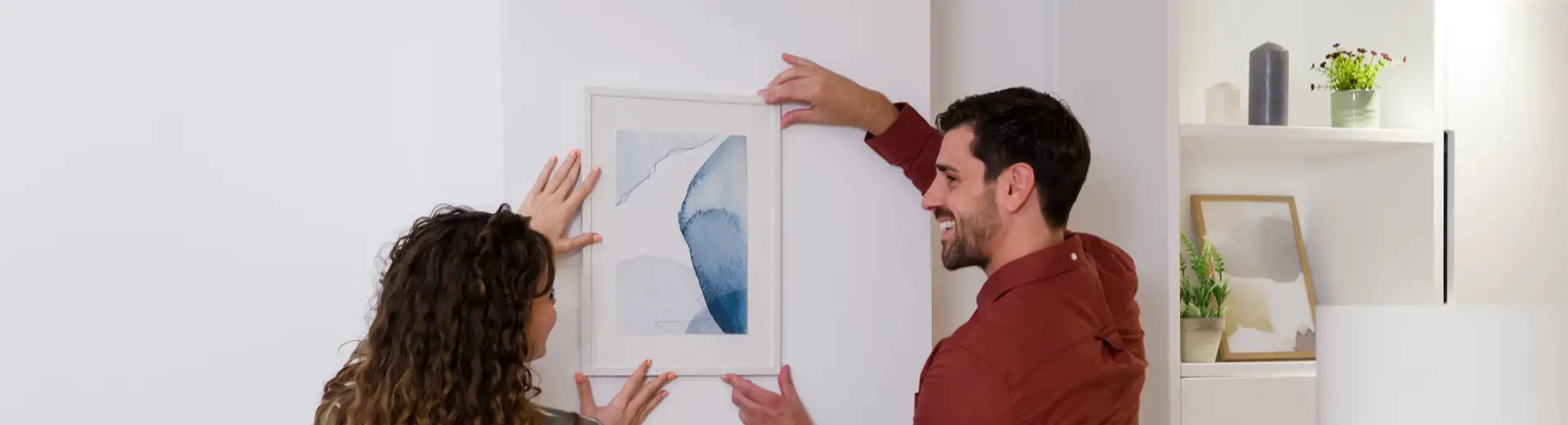 man and woman placing framed watercolor painting on wall