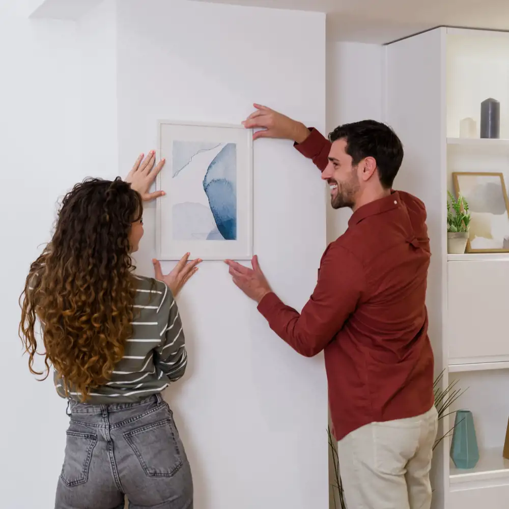 man and woman placing framed watercolor painting on wall