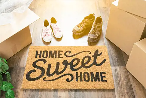 Image of floor mat reading "Home Sweet Home" and surrounded by shoes and moving boxes