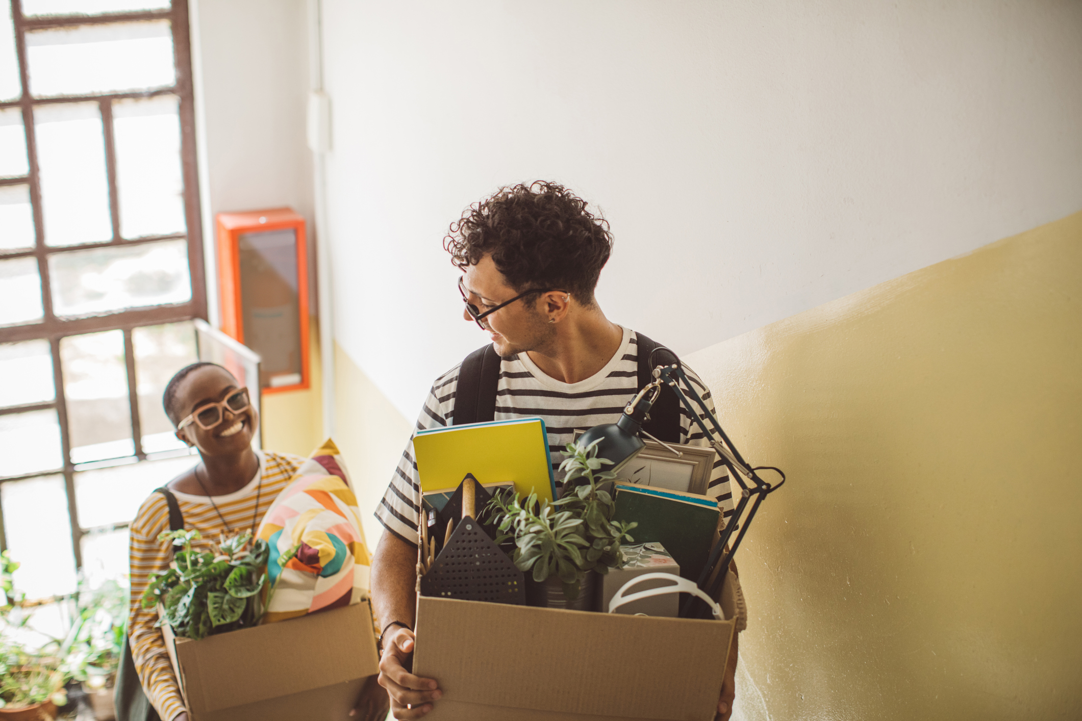 two roommates chatting while holding boxes of belongings and walking up stairs