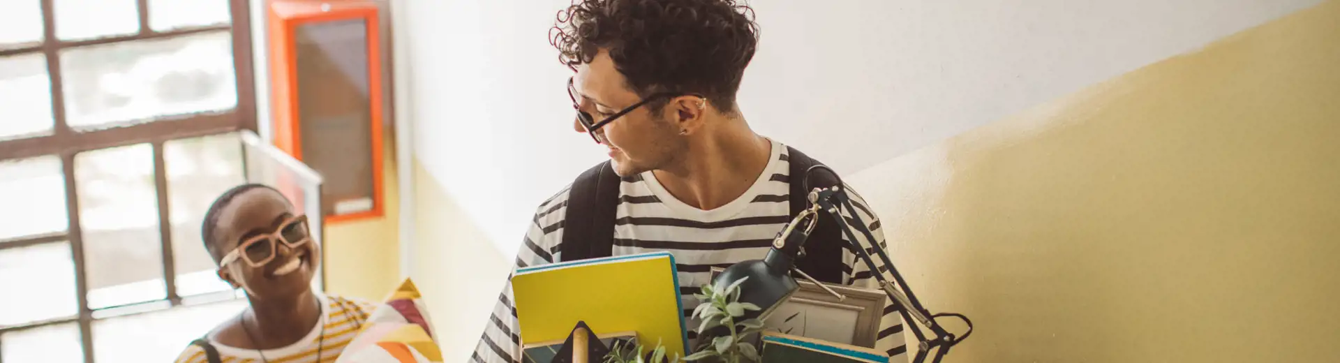 two roommates chatting while holding boxes of belongings and walking up stairs