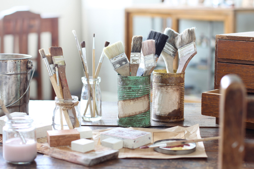 paint brushes in old cans and other artist's supplies on a wooden table