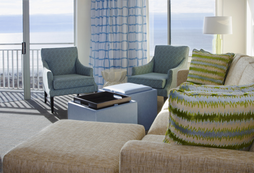 salon lumineux avec vue sur l’océan, fauteuils, canapé et coussins à motifs