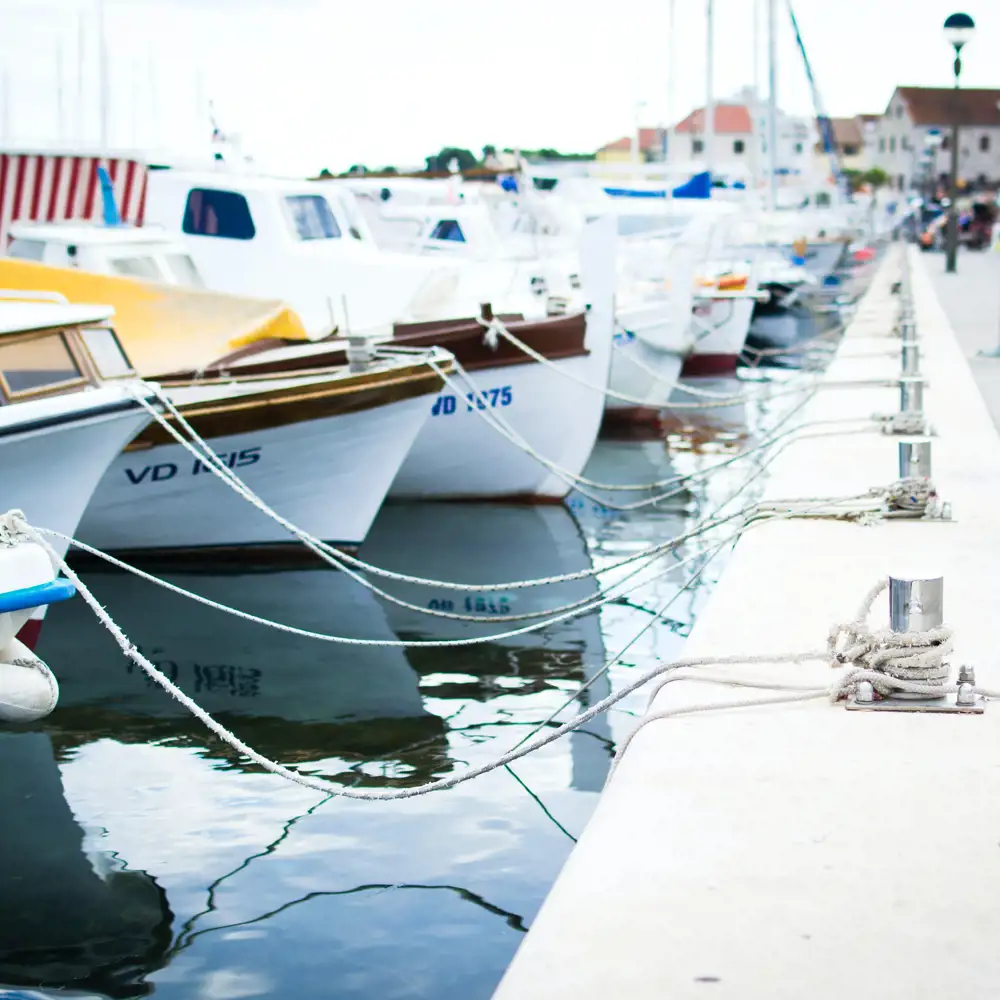 Multiple boats lined up in a row tied to a dock in the marina.