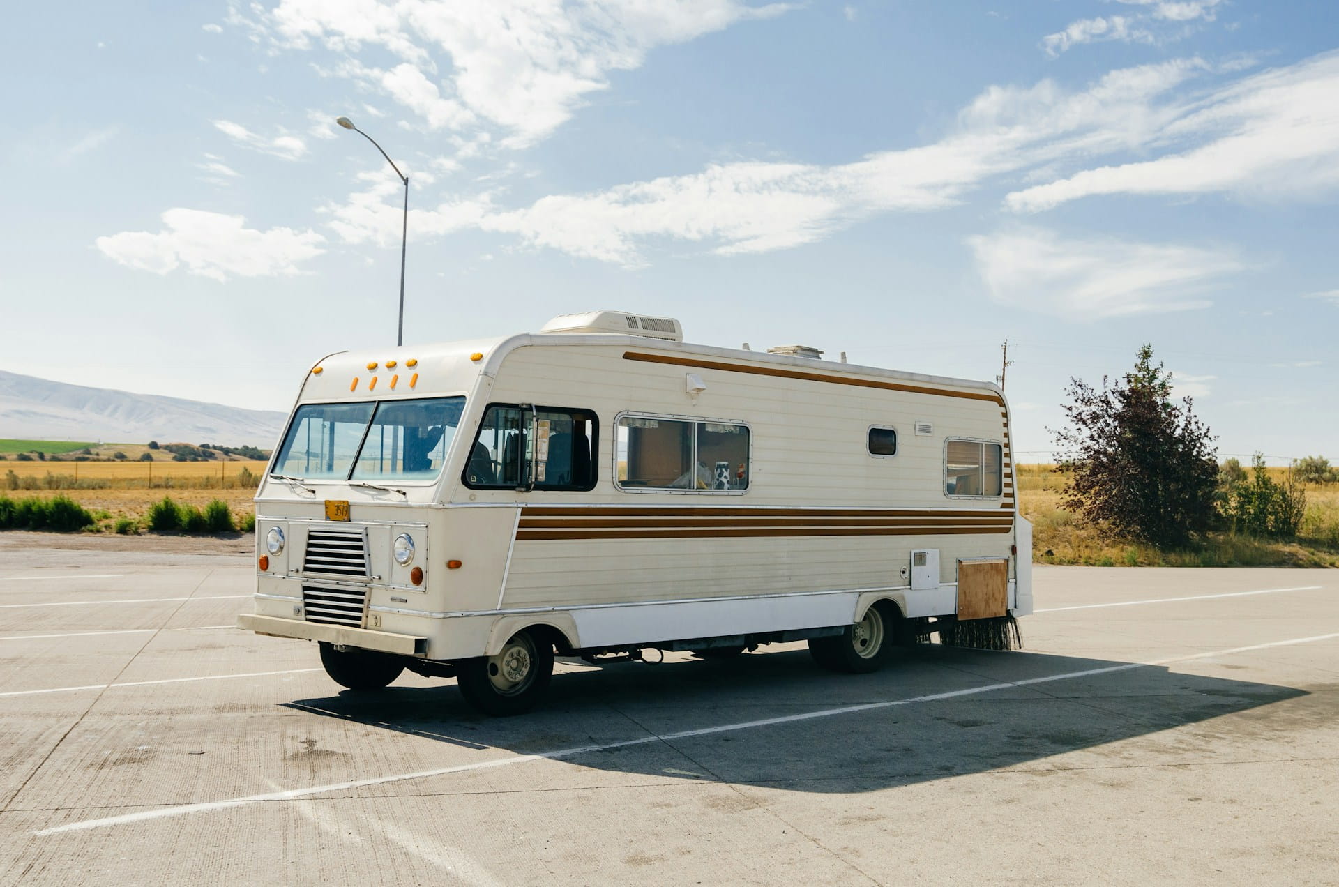 beige rv parked in empty parking lot on sunny day