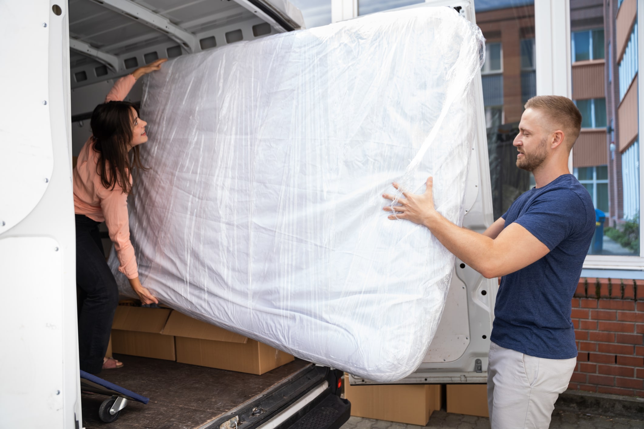 couple moving wrapped mattress into a moving truck