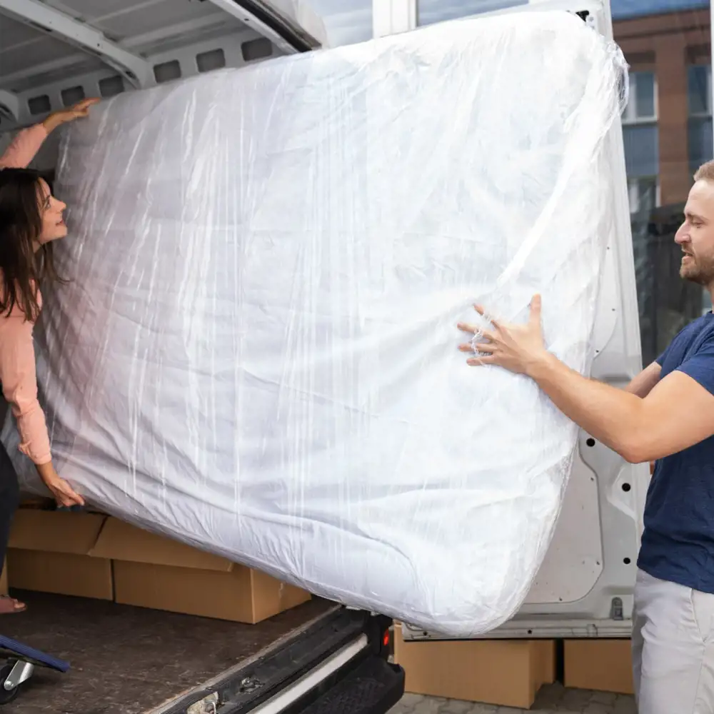 couple moving wrapped mattress into a moving truck