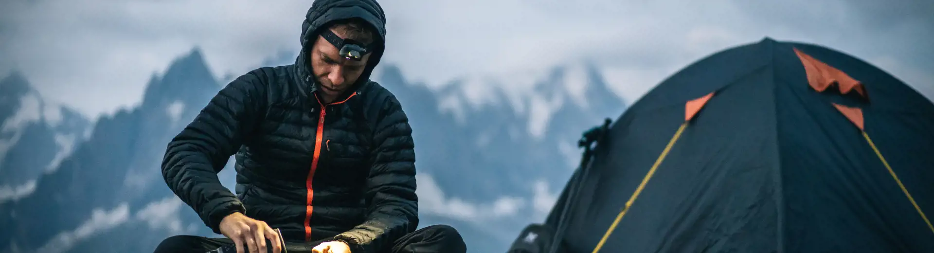 man pouring a drink outside of tent while camping in the mountains