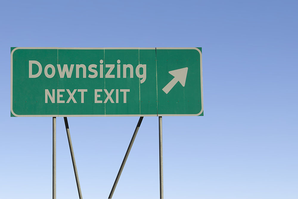 There is a green street sign that says “downsizing next exit” while pointing to the right.