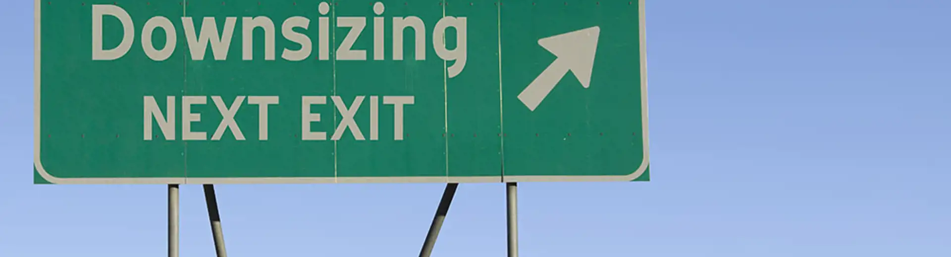 There is a green street sign that says “downsizing next exit” while pointing to the right.
