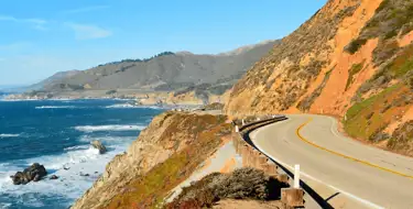 Image of winding road along the ocean with mountains in distance