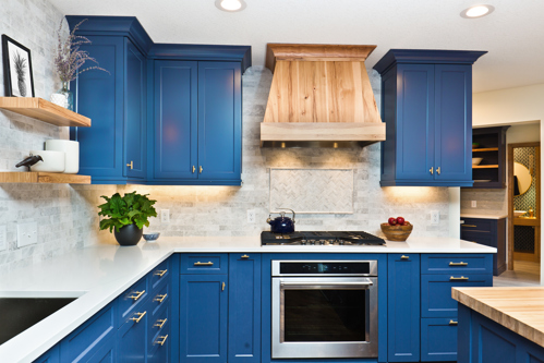 modern kitchen with blue cabinets, wooden range hood, and stainless steel oven