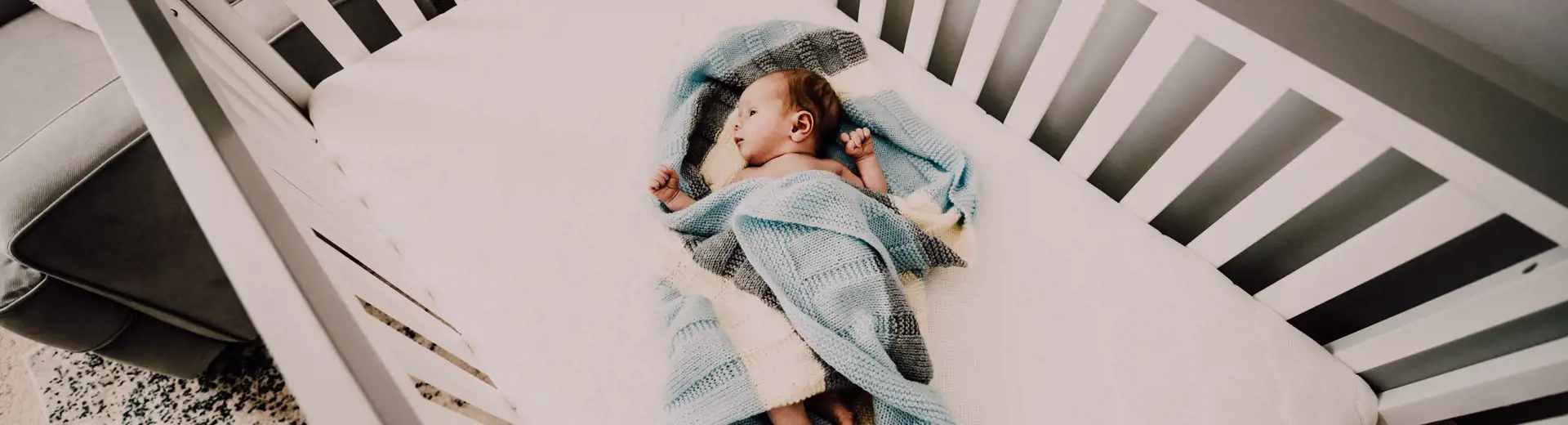 Un bébé enveloppé dans une couverture bleue, couché dans un berceau et regardant un mobile.