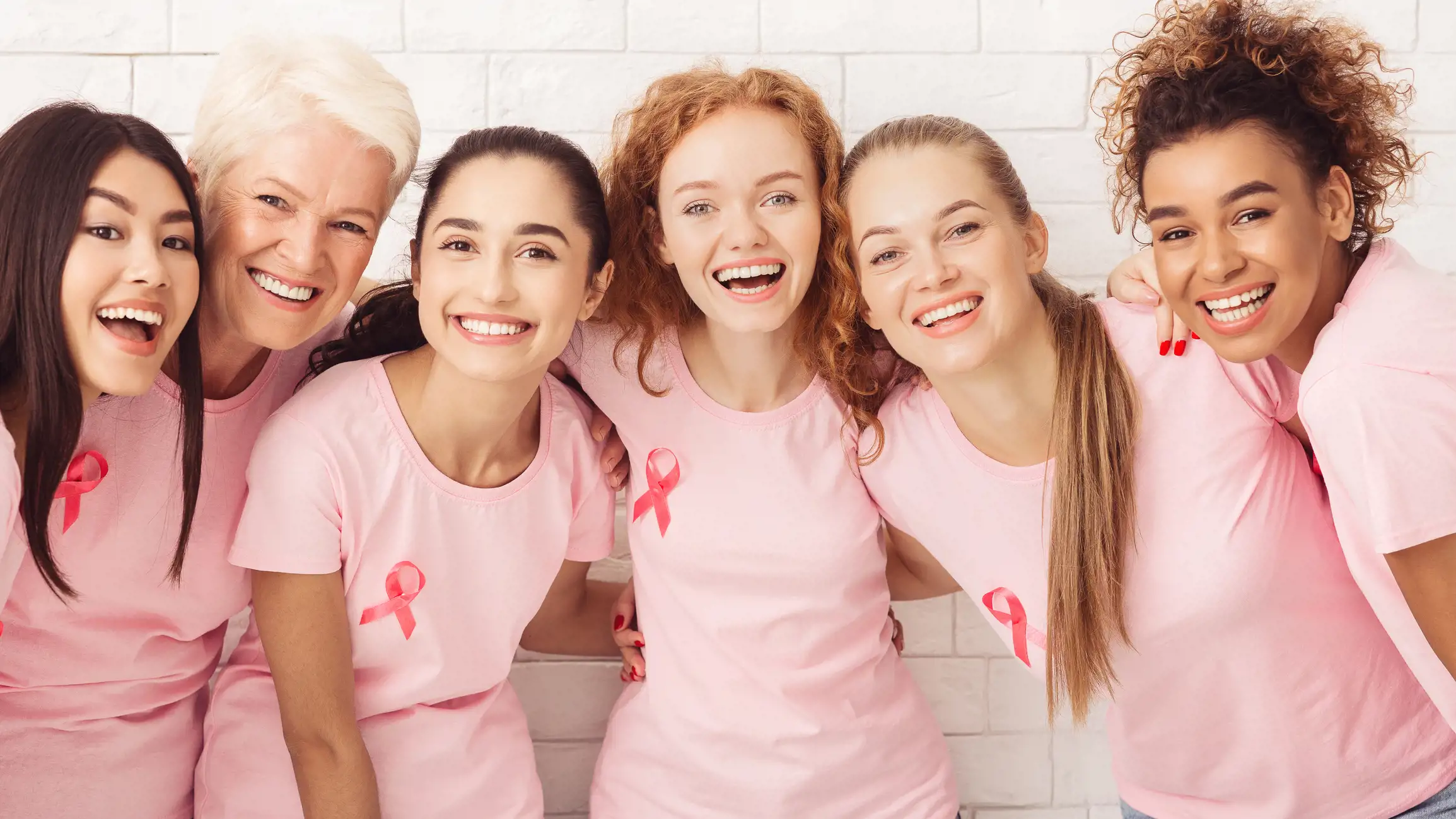 Six happy women huddling together for Breast Cancer Awareness