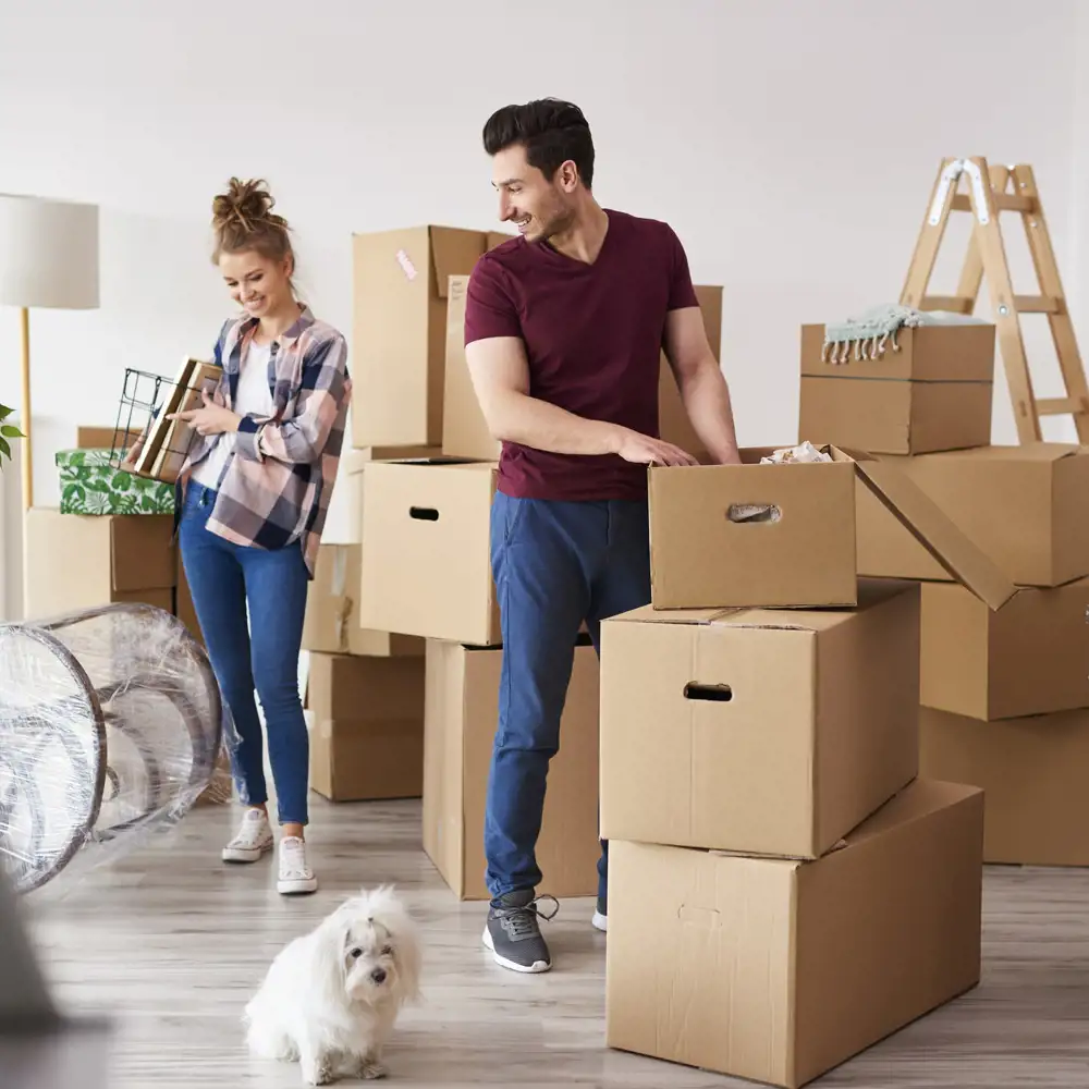 couple with small dog carrying boxes while moving into new home