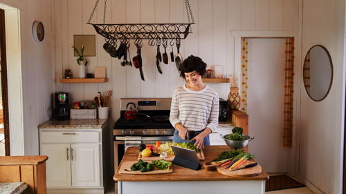 person preparing food at a kitchen island with fresh vegetables and hanging cookware