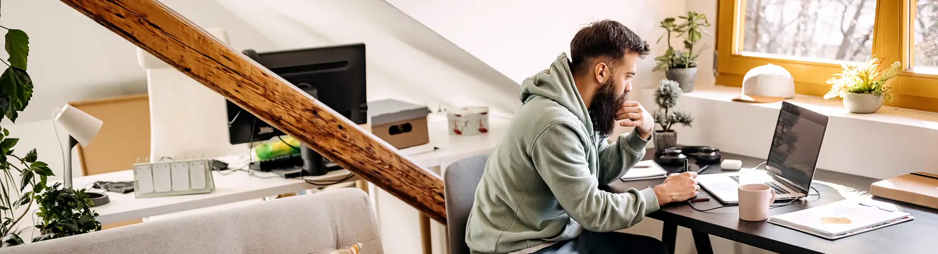 man in a small apartment working at his desk with dog resting at his feet