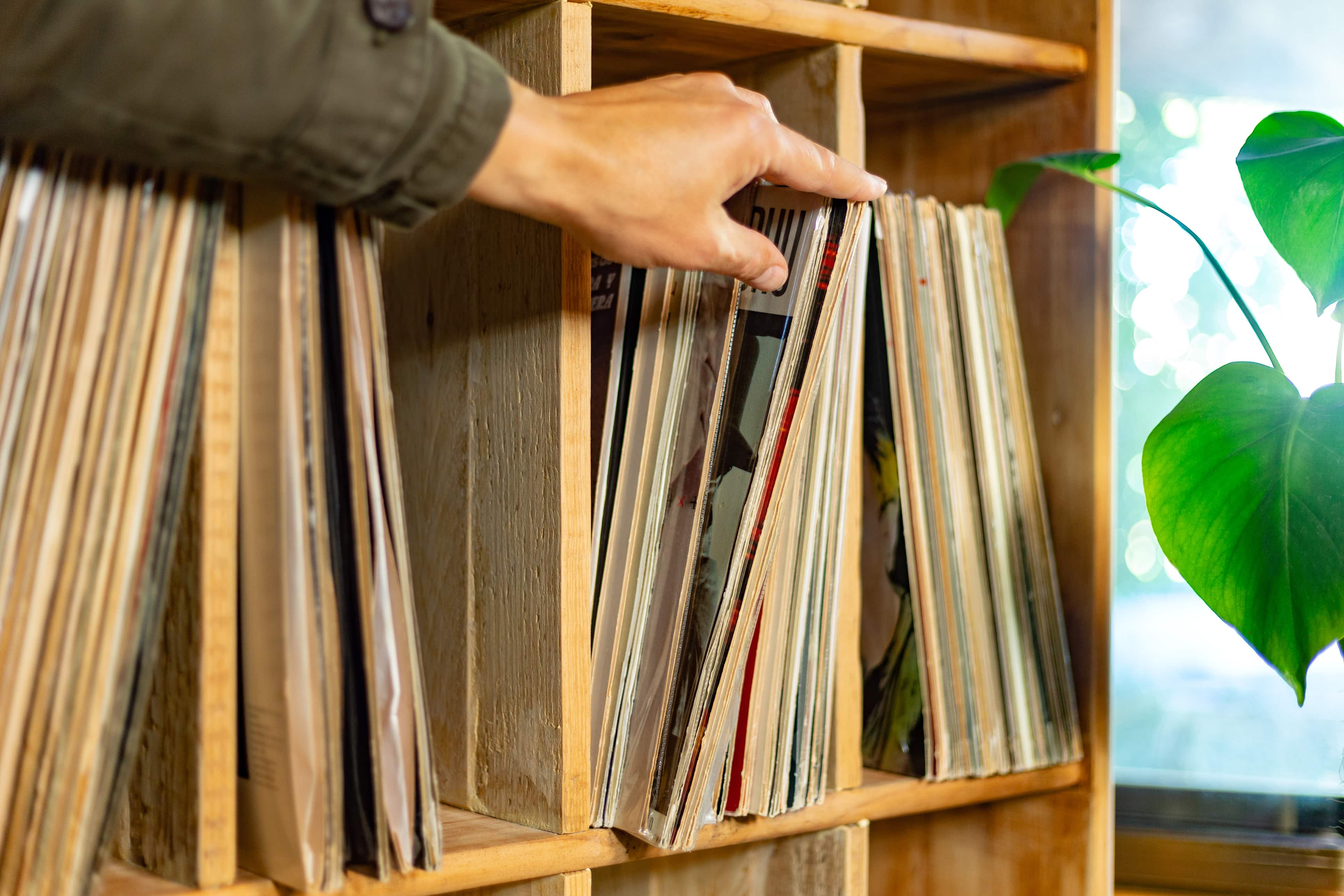 person pulling vinyl record off wooden shelf