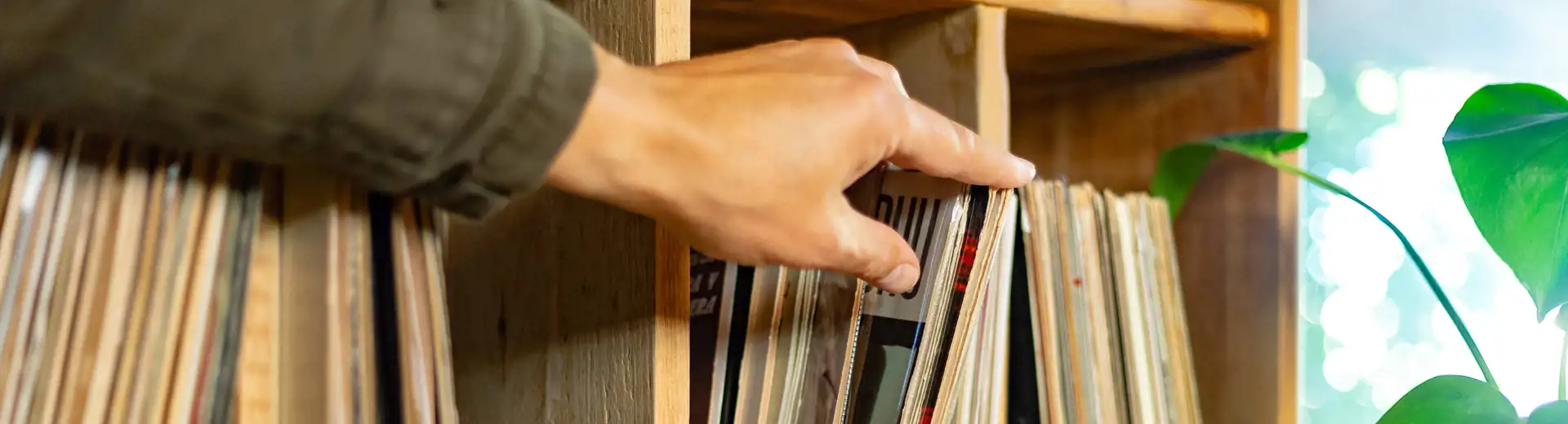 person pulling vinyl record off wooden shelf