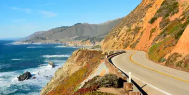 Image of winding road along the ocean with mountains in distance