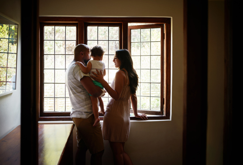 Couple with their young child looking outside the window of the home