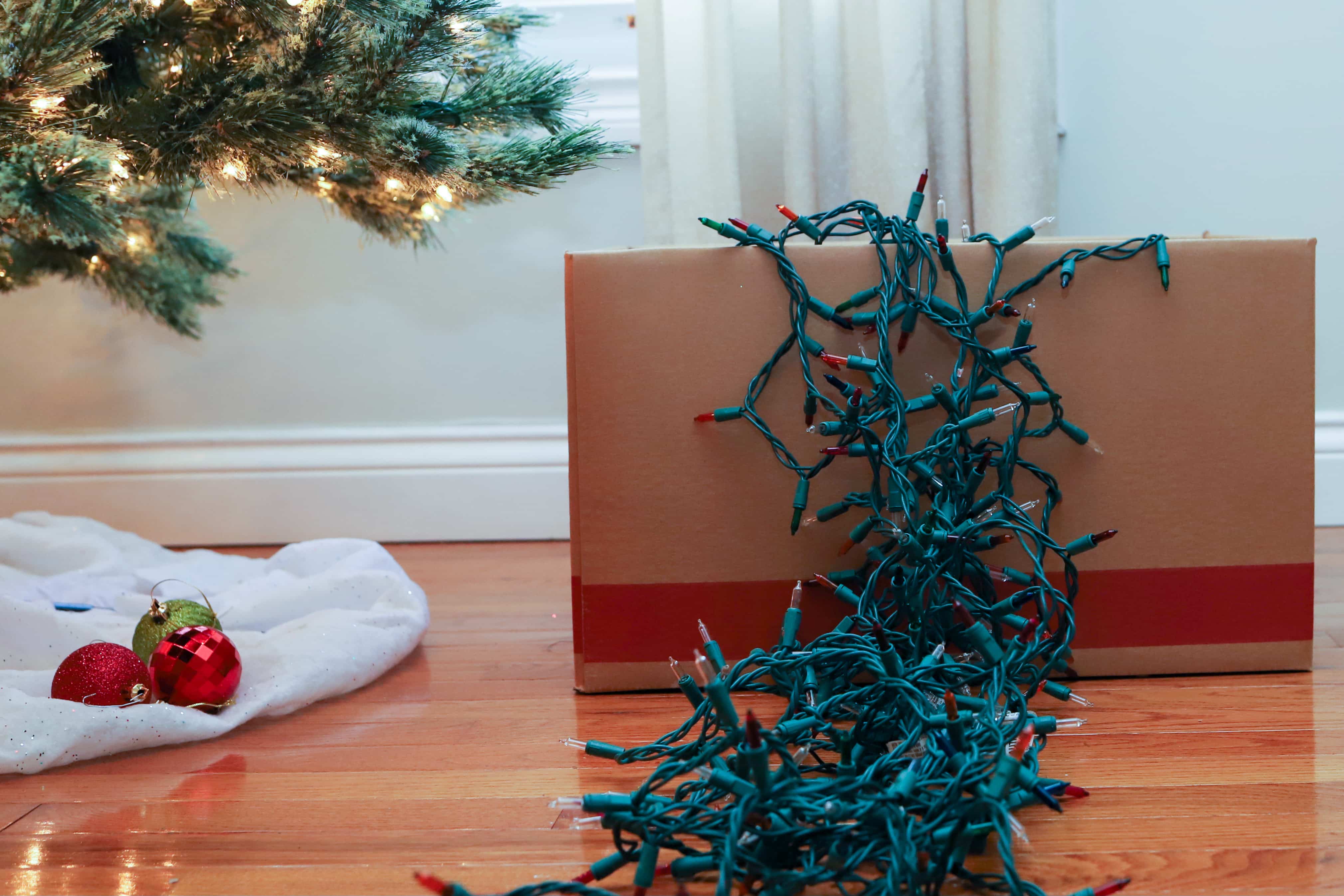 cardboard box with string lights spilling out over top next to christmas tree