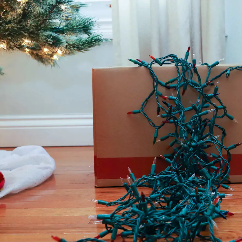 cardboard box with string lights spilling out over top next to christmas tree