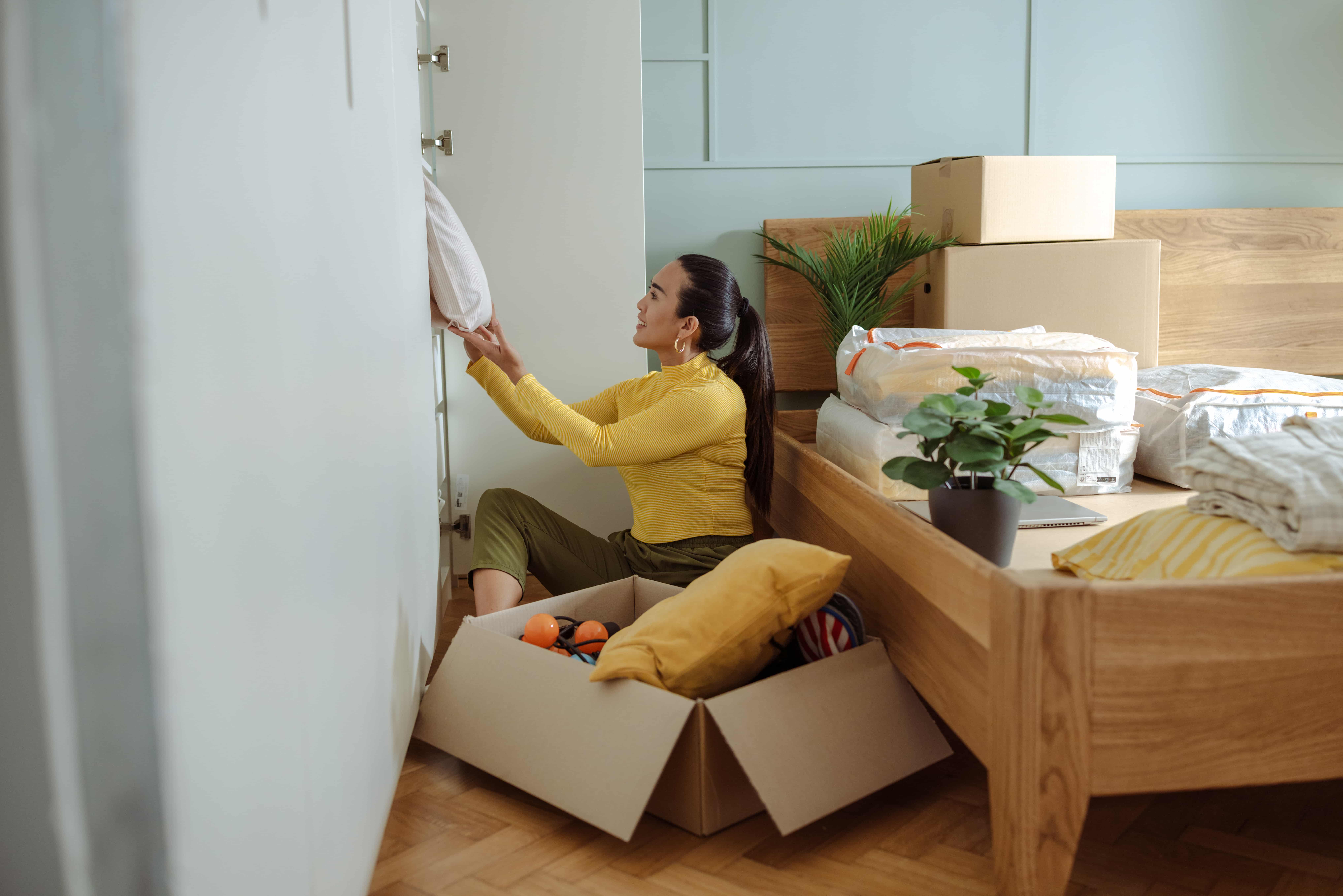 woman sitting in bedroom organizing closet items into boxes