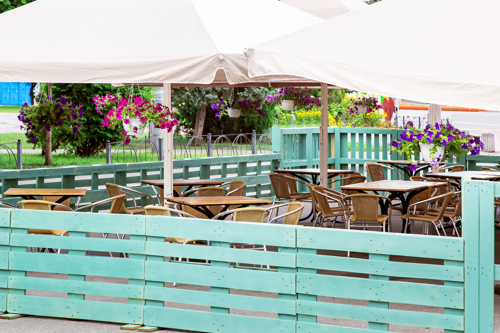 outdoor café seating area with tables, chairs, and hanging flower baskets under a canopy